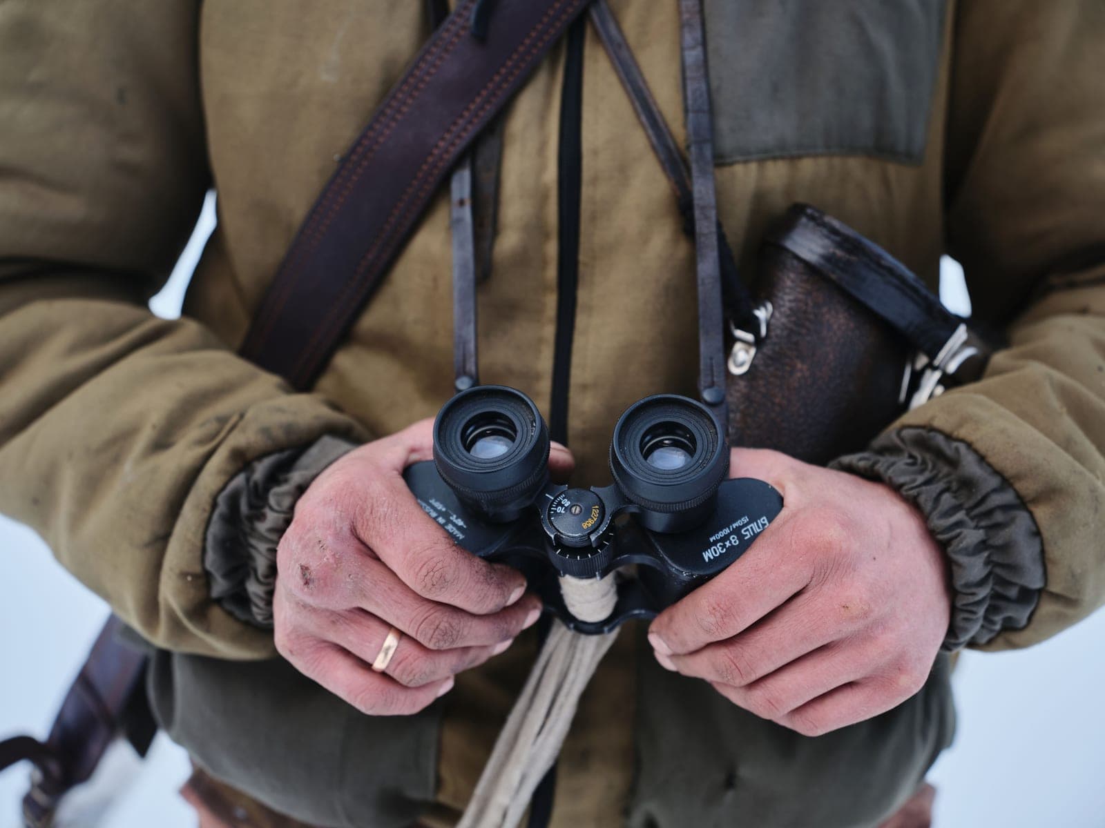 Binoculars held against a jacket on a chest harness strap.