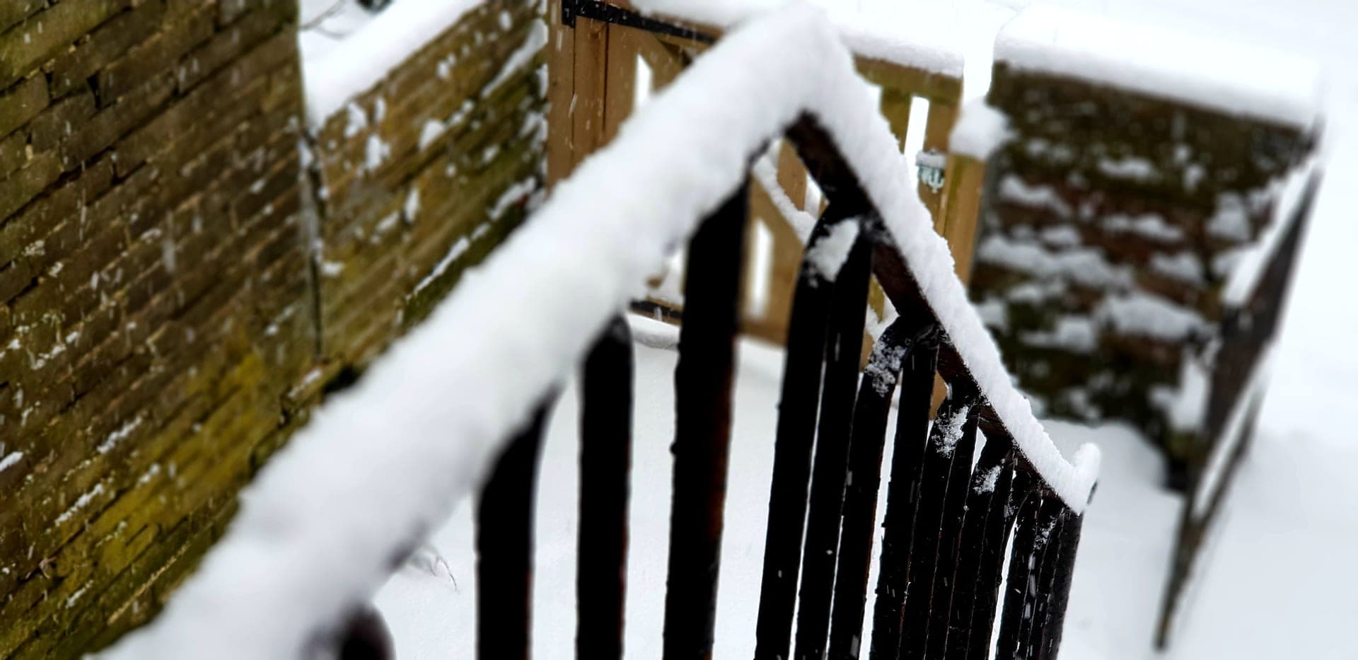 A snow-covered wooden deck railing running away from the camera on a gray day.