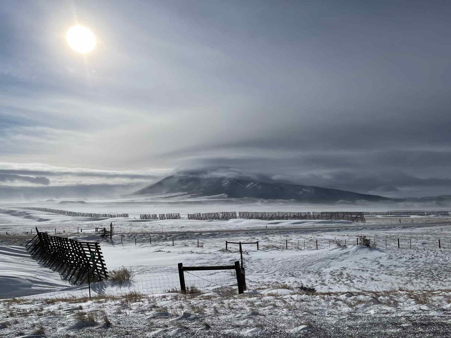 Wind driving loose snow across an open winter field.