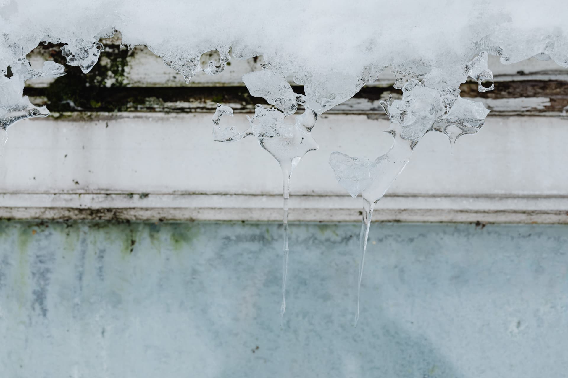 Icicles hanging in a row from a frozen edge against a pale winter sky.