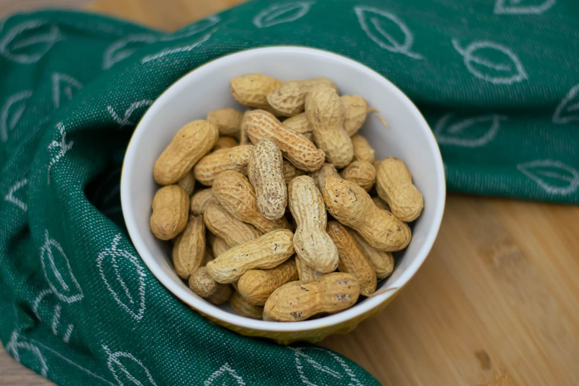 Shelled peanuts in a shallow wooden bowl, seen from above.