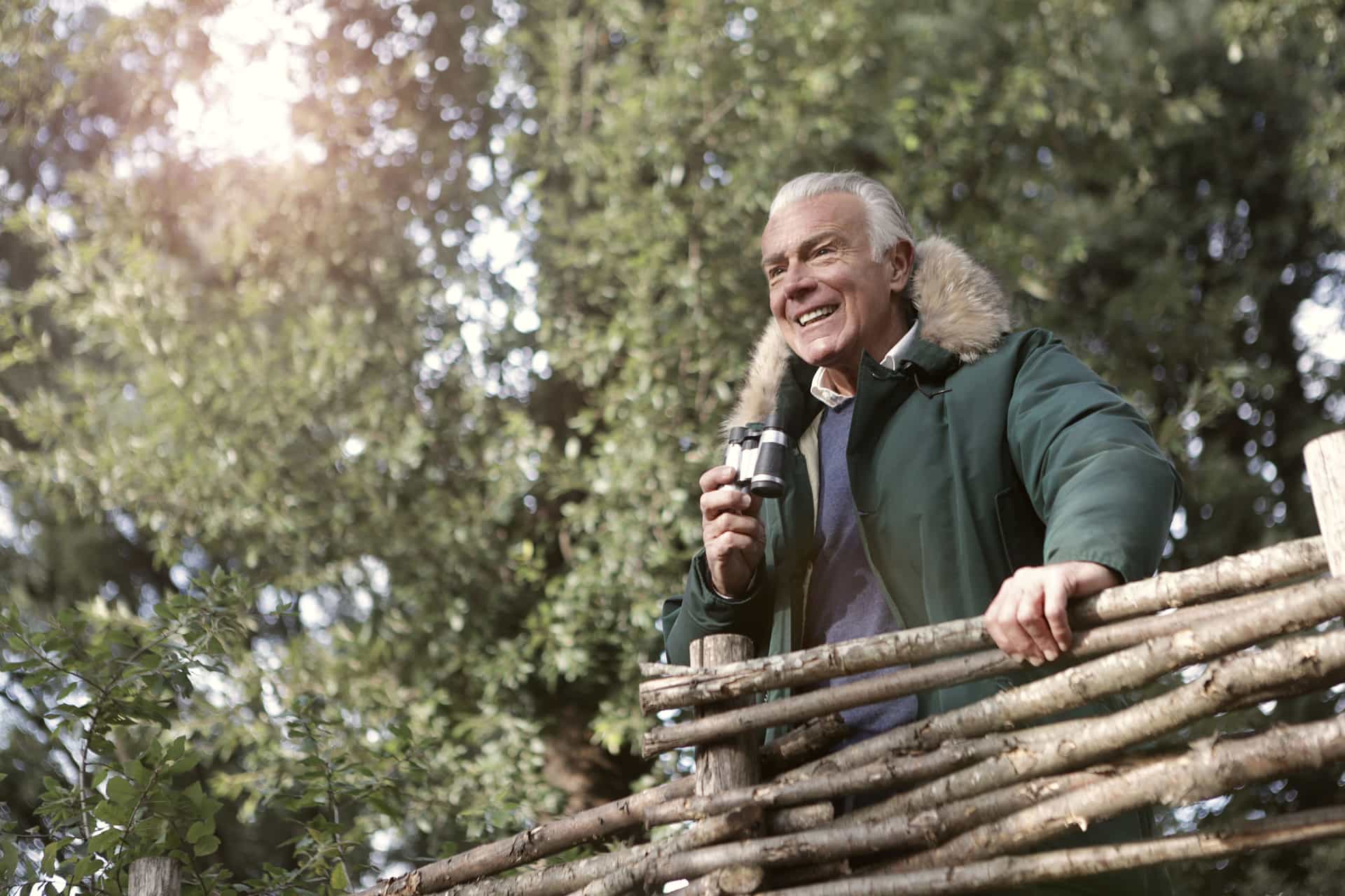 A birder with binoculars raised, standing at the edge of a snow-covered woodland.